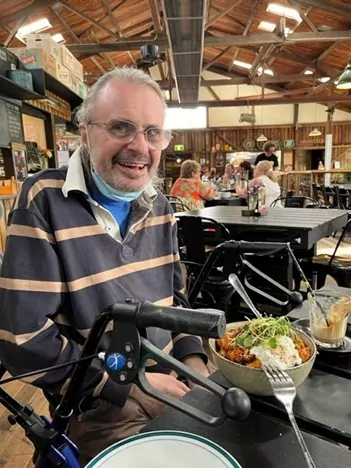 Man smiling at restarant with food and wheely walker
