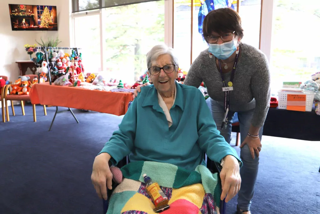 Carer stands behind a woman in a wheel chair.