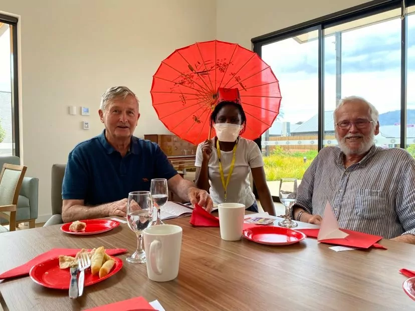 A woman with a red umbrella sits at a table with a man on either side